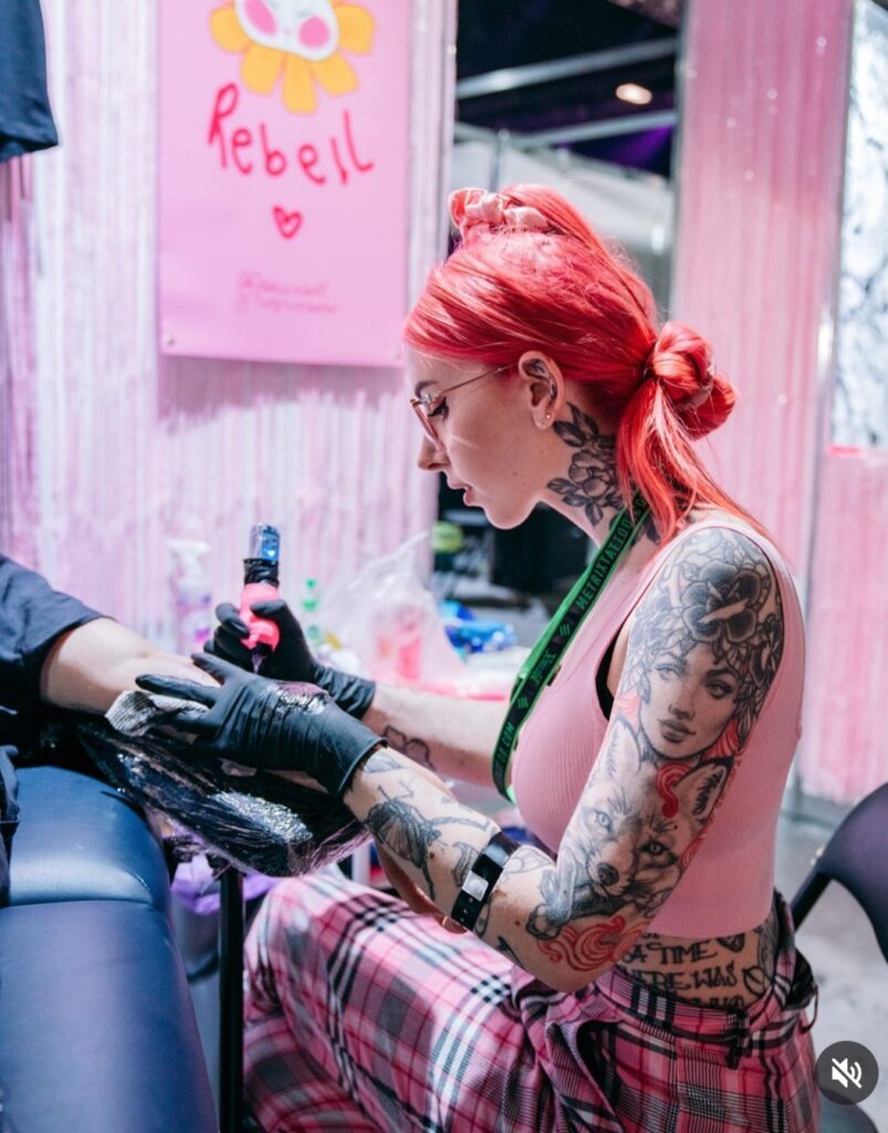 Jessica Rebell tattooing at her stand at the tatoo convention. There is a lot of pink!